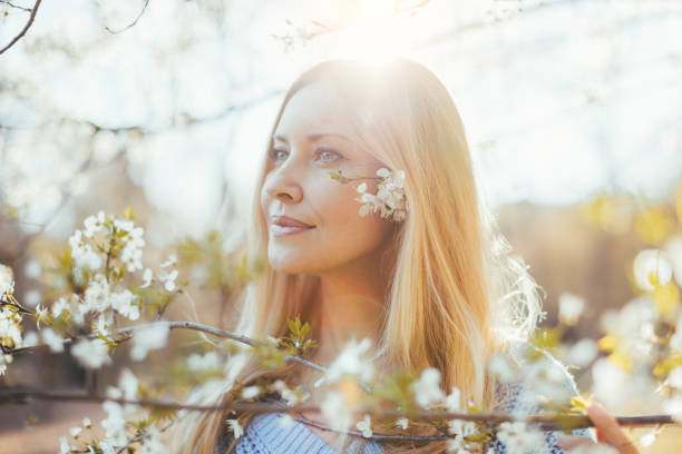 hermoso cabello rubio de mediana edad mujer posando con árbol de jazmín en flor - women spring sensuality fashion model fotografías e imágenes de stock