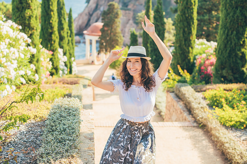Young attractive woman tourist posing in beautiful garden - smiling girl enjoying summer wearing panama hat