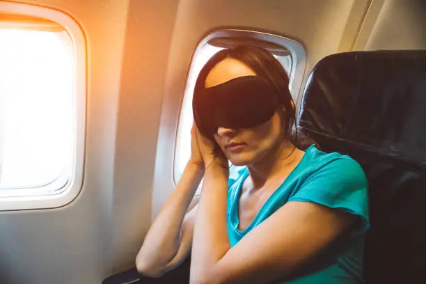 Photo of Young woman sleeping on a plane with black eye mask on her face - tired girl resting during a long flight - jet lag concept