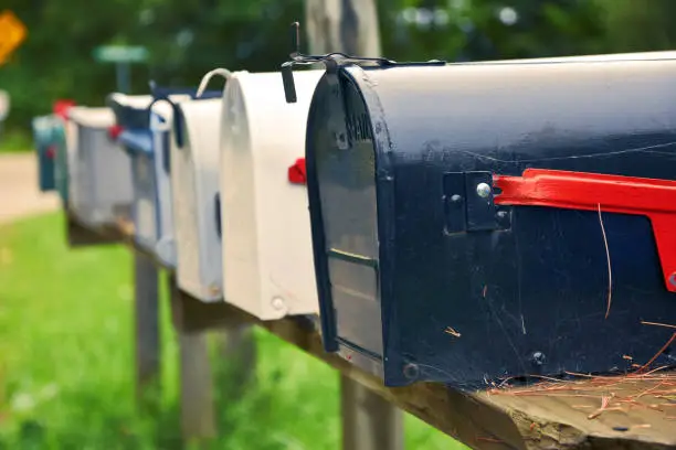 Photo of An isolated row of metal US mail boxes on wooden post in the countryside. Spider webs in one of them. Mail concept. New York City. United States