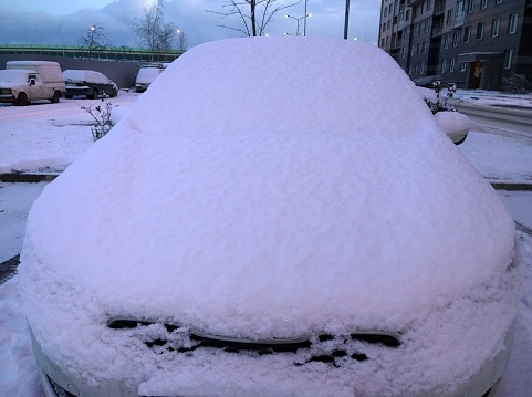 Snow covered car in winter. Danger by not clearing auto of ice. Winter is here. Frosty cold weather, blizzard, snowstorm. Snowfall in the city. Protection of vehicle against corrosion, salt, reagents.