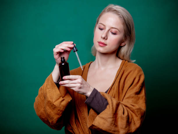 blonde frau mit schwarzer flasche und pipette auf grünem hintergrund - jar human hand moisturizer packaging stock-fotos und bilder