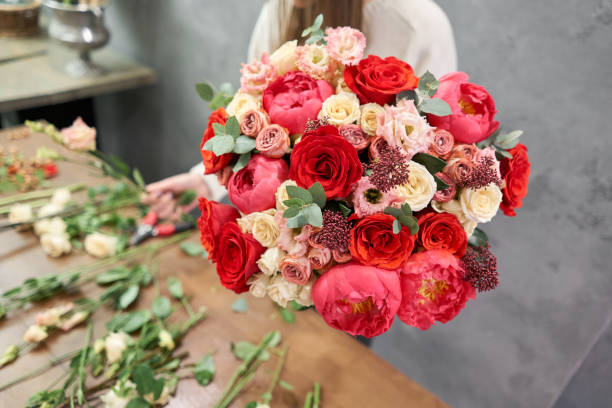 concepto de tienda floral europea. mujer florista crea rojo hermoso ramo de flores mixtas. un grupo fresco y guapo. cursos de educación, clasemagistrals y floristería. entrega de flores. - florist women bouquet spring fotografías e imágenes de stock