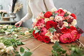 European floral shop concept. Florist woman creates red beautiful bouquet of mixed flowers. Handsome fresh bunch. Education, master class and floristry courses. Flowers delivery.