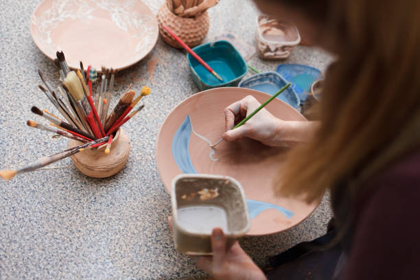 istock Potter woman paints a ceramic plate. Girl draws with a brush on earthenware. Process of creating clay products 1194160724
