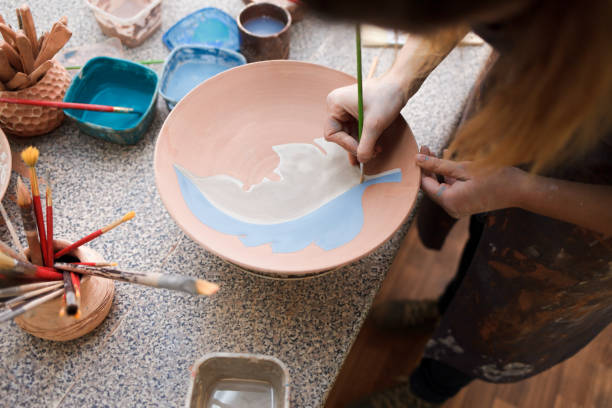 istock Potter woman paints a ceramic plate. Girl draws with a brush on earthenware. Process of creating clay products 1194161257