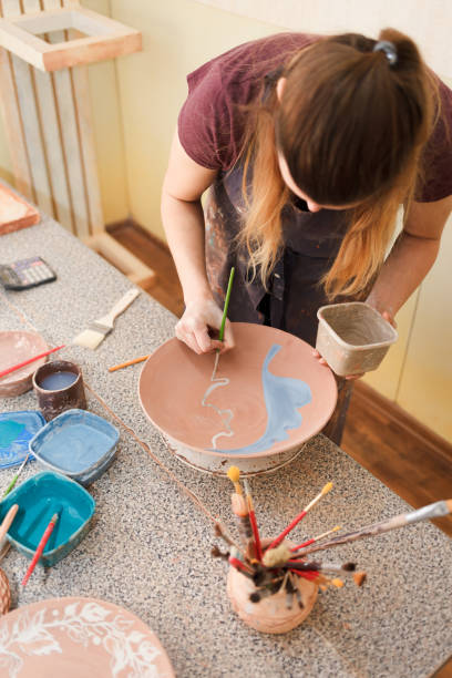 istock Potter woman paints a ceramic plate. Girl draws with a brush on earthenware. Process of creating clay products 1194161302