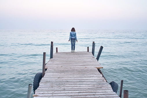 Woman standing on old wooden pier and watching on water sea