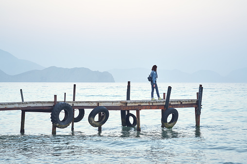 Woman walking on old wooden pier and watching on water sea