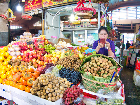 A trader checks her mobile phone with fruit and vegetables for sale at a market stall in Phnom Penh, Cambodia