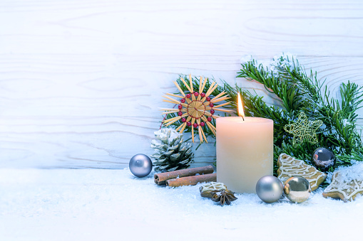 Burning candle and Christmas decoration on snow against a white wooden background, copy space, selected focus, narrow depth of field
