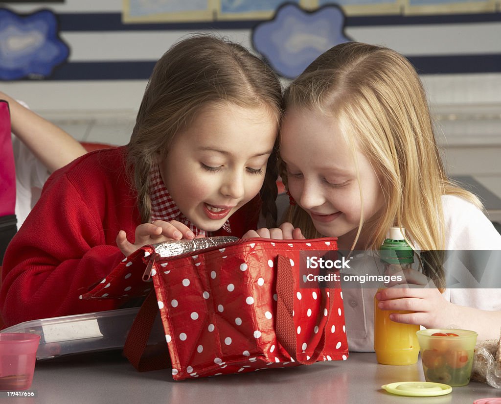 Dos niñas echar un vistazo en el almuerzo bolsa de clase - Foto de stock de Almuerzo en lonchera libre de derechos