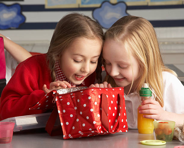Two little girls peeking into lunch bag in class stock photo
