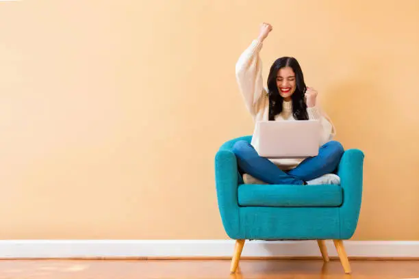 Young woman with a laptop computer with successful pose sitting in a chair