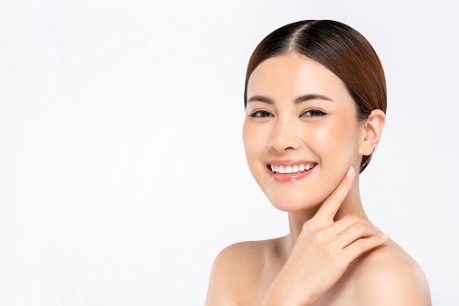 Youthful bright skin smiling pretty Asian woman with hand touching face on white background for beauty concepts