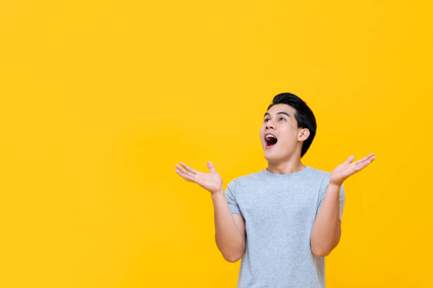 Excited Asian man gasping with hands open Excited Asian man gasping with hands open and looking to copy space isolated on yellow background male meaning stock pictures, royalty-free photos & images