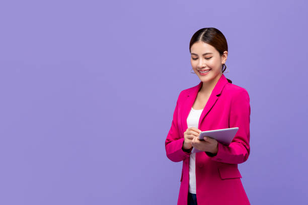 Smart beautiful Asian woman in pink business suit using digital tablet Smart beautiful Asian woman in pink business suit using digital tablet isolated on purple background blazer jacket stock pictures, royalty-free photos & images