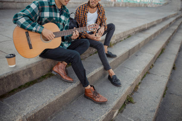 istock Smiling two male friends sitting on steps with guitar 1194190637