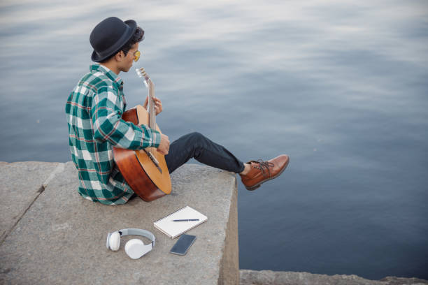 istock Young musician sitting with guitar near river 1194191699