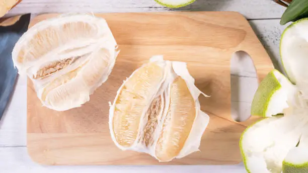 Photo of Fresh peeled pomelo, pummelo, grapefruit, shaddock on bright wooden background. Autumn seasonal fruit, top view, flat lay, tabletop shot.