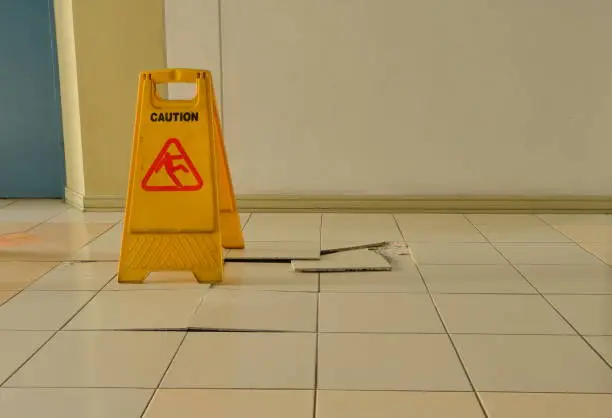 Closeup buckled and broken tiles on corridor near elevator with a caution sign for warning and protecting people from stepping on them