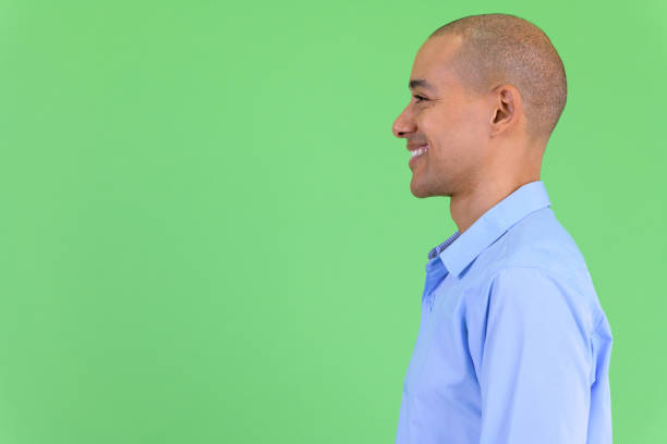 Closeup profile view of happy bald multi ethnic businessman smiling Studio shot of handsome bald multi ethnic businessman against green background balding photos stock pictures, royalty-free photos & images