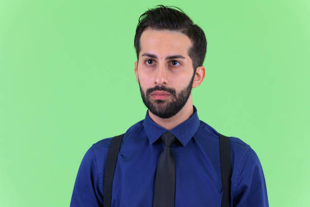 Studio shot of young handsome bearded Persian businessman against green background