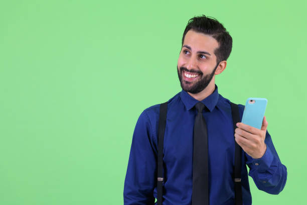 istock Young happy bearded Persian businessman thinking while using phone 1194199503