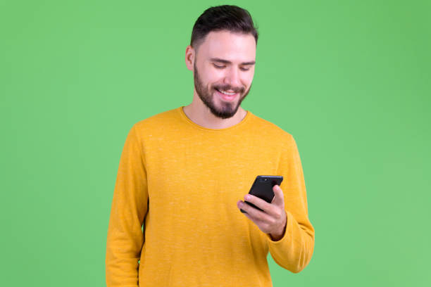 Happy young handsome bearded man using phone