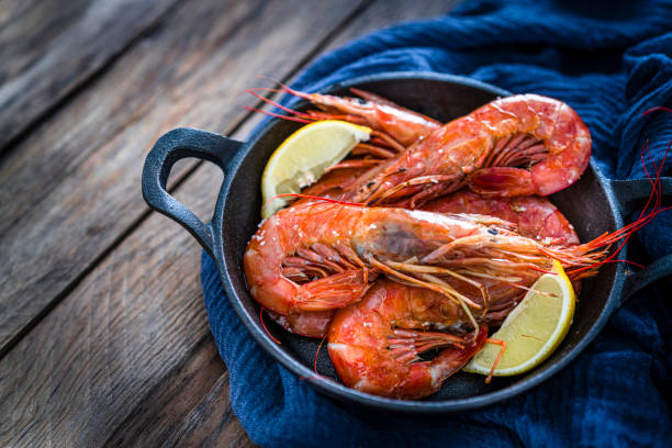 camarones cocidos en una sartén de hierro fundido rodado sobre una mesa de madera. copiar espacio - camarón marisco fotografías e imágenes de stock