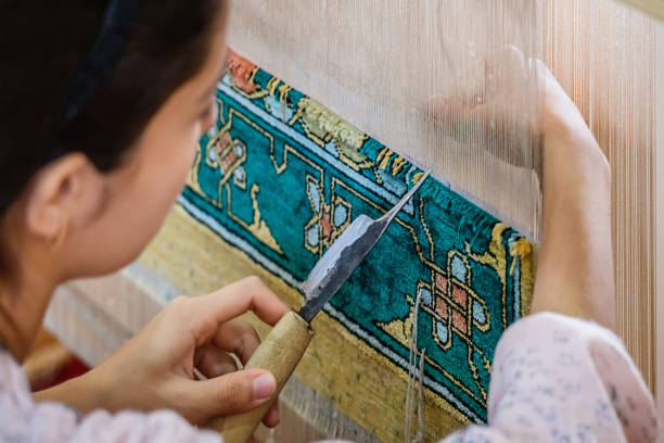 Bukhara, Uzbekistan - October 30th, 2019: Female uzbek silk carpet knotting and tying - weaving a arabian-oriental uzbek silk carpet. Uzbek Silk Carpet Workshop. Typical Carpet - Textile Handicraft in Bukhara - Buxoro - Бухорo, Silk Road, Khorezm Region, Uzbekistan, Central Asia.