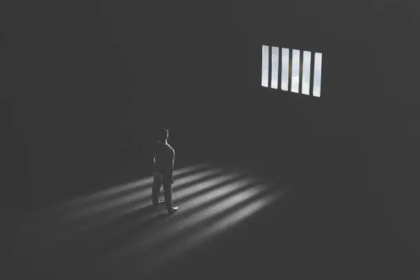 Photo of jail window light in a completely dark prison cell illuminated guilty man
