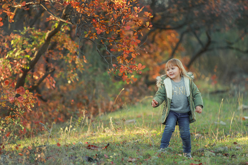 Funny kid girl pretending to be posing in autumn forest, wearing a green coat.