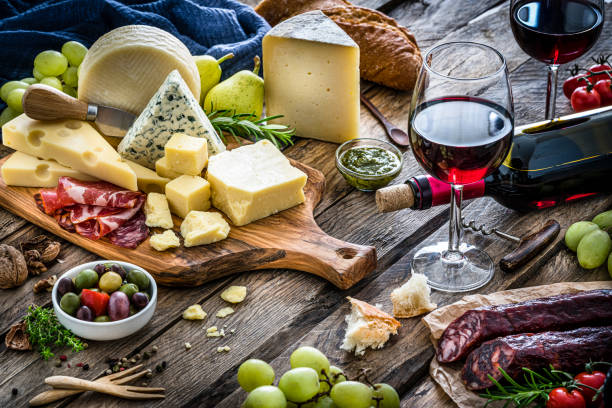 Appetizer: red wine, cheese and cured ham on rustic wooden table High angle view of delicious appetizer shot on rustic wooden table. The composition includes a selection of cheeses, Iberico ham, Spanish chorizo, red wine, grapes, olives and bread. Predominant colors are red, yellow and brown. XXXL 42Mp studio photo taken with Sony A7rii and Sony FE 90mm f2.8 macro G OSS lens wine italian culture wine bottle bottle stock pictures, royalty-free photos & images