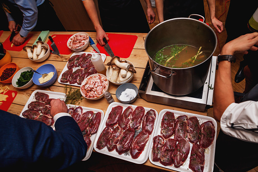 Process of cooking meat and soup at masterclass in restaurant. Hands of several people performing various actions.