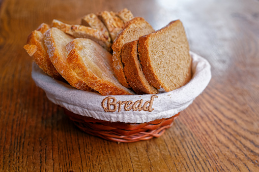 Basket of white bread and wholegrain bread slices on a wooden table under natural daylight. Bread text written on the basket.