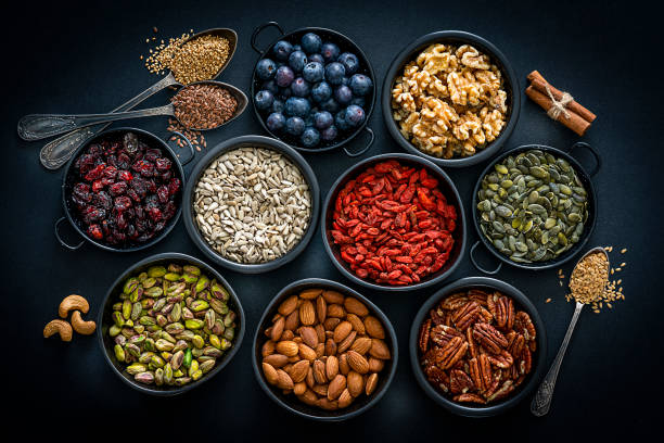 Healthy eating: assortment of nuts, seeds and fruits. Top view. Healthy eating: top view of several small bowls filled with nuts, seeds and fruits sitting on black background. The composition includes blueberries, goji berries, pecan, pumpkin seeds, walnuts, almonds, sunflower seeds, cinnamon sticks and cashew. High resolution 42Mp studio digital capture taken with Sony A7rii and Sony FE 90mm f2.8 macro G OSS lens antioxidant stock pictures, royalty-free photos & images