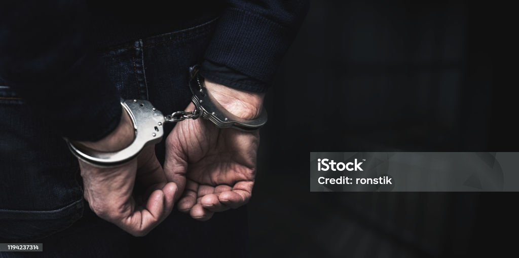 handcuffed arrested man behind prison bars. copy space Arrest Stock Photo