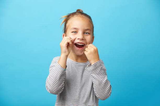 little girl brushing her teeth with dental floss. Portrait of smiling little five years old girl brushing her teeth with dental floss on blue isolated background. dental floss stock pictures, royalty-free photos & images