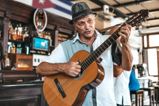 An old man with hat playing an acoustic guitar in a bar in Havana, Cuba.