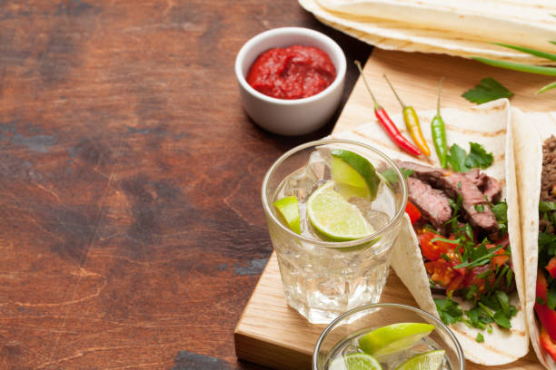 Set of mexican tacos with meat and vegetables in tortilla. And caipirinha cocktail. On wooden table. With copy space