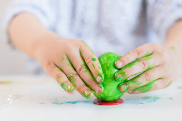 istock A child puts a green Easter egg on a stand with his hands stained with paint on a white table. 1194242462