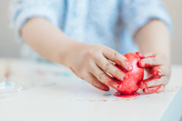 istock A child puts a red Easter egg on a stand with his hands stained with paint on a white table. 1194242720