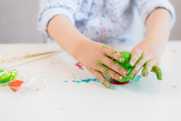istock A child puts a green Easter egg on a stand with his hands stained with paint on a white table. 1194243298