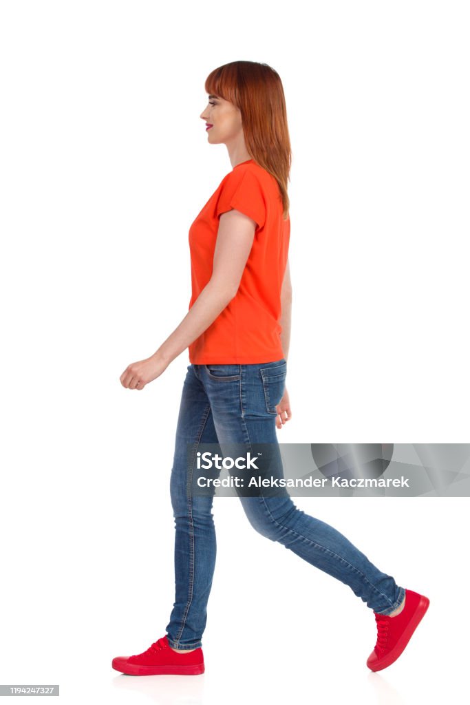 Walking Woman In Orange Tshirt Jeans And Red Sneakers Side View