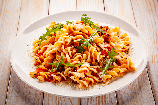 Fusilli with pork, sauce and vegetables on color gradient background