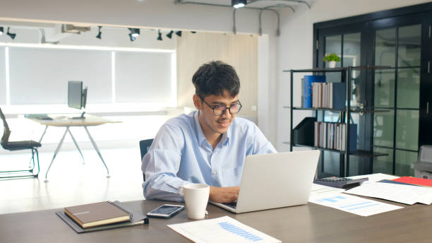 istock Young asian businessman smiling while working with laptop computer at office, business office lifestyle concept 1194248860