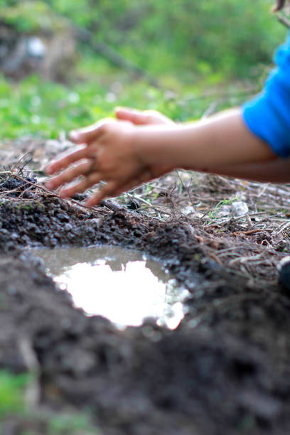 istock child playing with mud - blur hands for focus on pond 1194253288