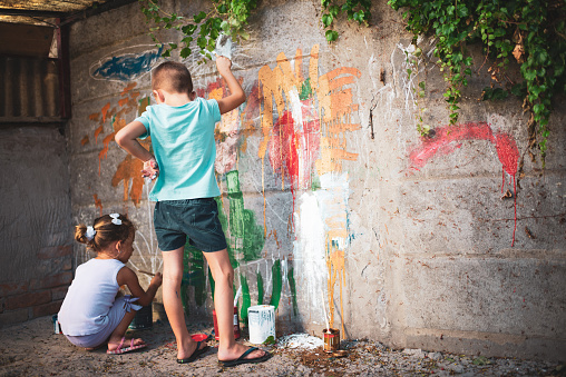 Cheerful little children having fun painting flowers on the wall.