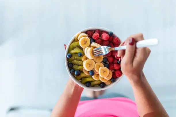Photo of Woman's hands holding a bowl with fresh fruit while standing at home.